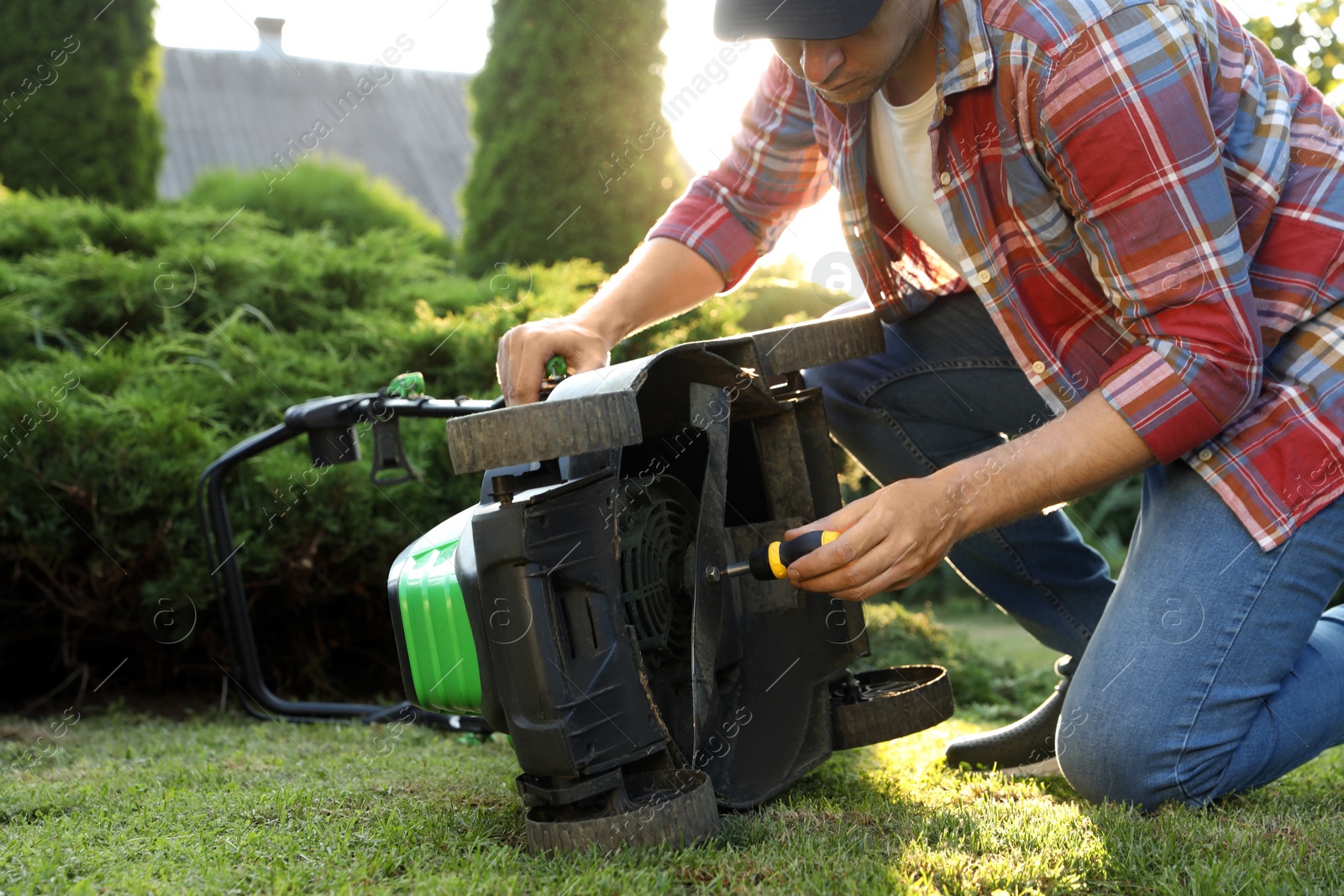 Photo of Man with screwdriver fixing lawn mower in garden, closeup