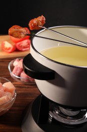 Photo of Fondue pot, forks with fried meat pieces and other products on wooden table, closeup