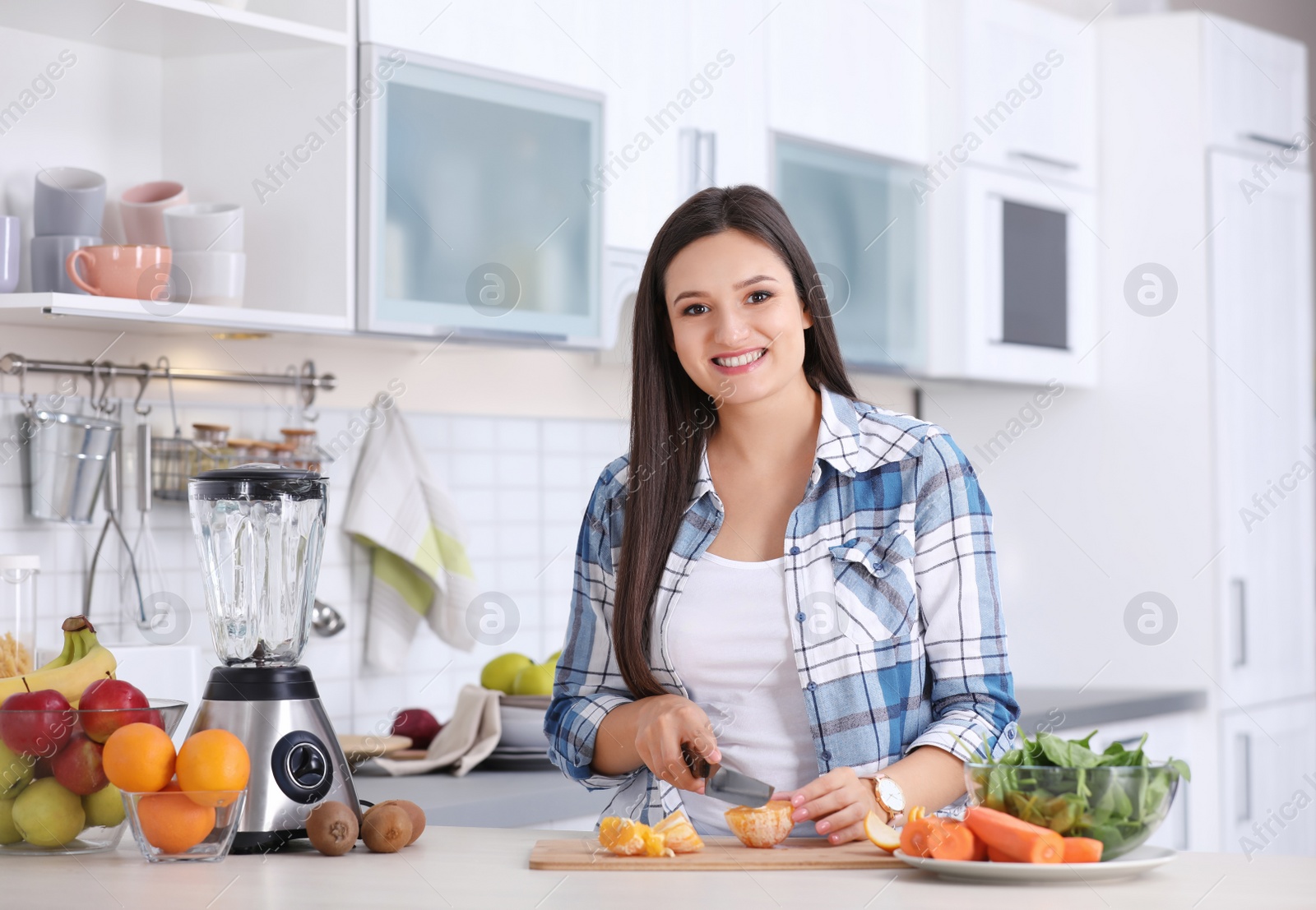 Photo of Young woman preparing tasty healthy smoothie at table in kitchen