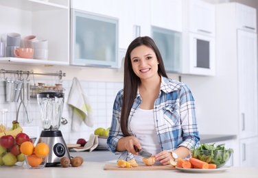 Young woman preparing tasty healthy smoothie at table in kitchen