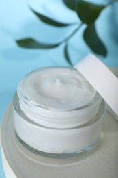 Photo of Jar of body cream with white stand on turquoise background, closeup