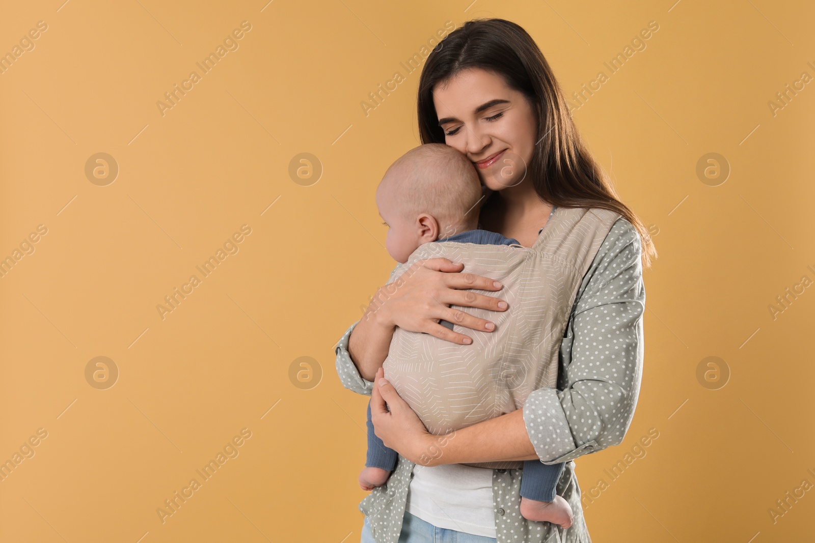 Photo of Mother holding her child in sling (baby carrier) on beige background. Space for text