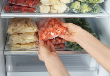 Photo of Woman taking plastic bag with frozen carrot from refrigerator, closeup
