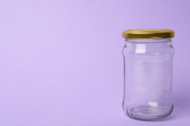 Photo of Closed empty glass jar on lilac background, space for text