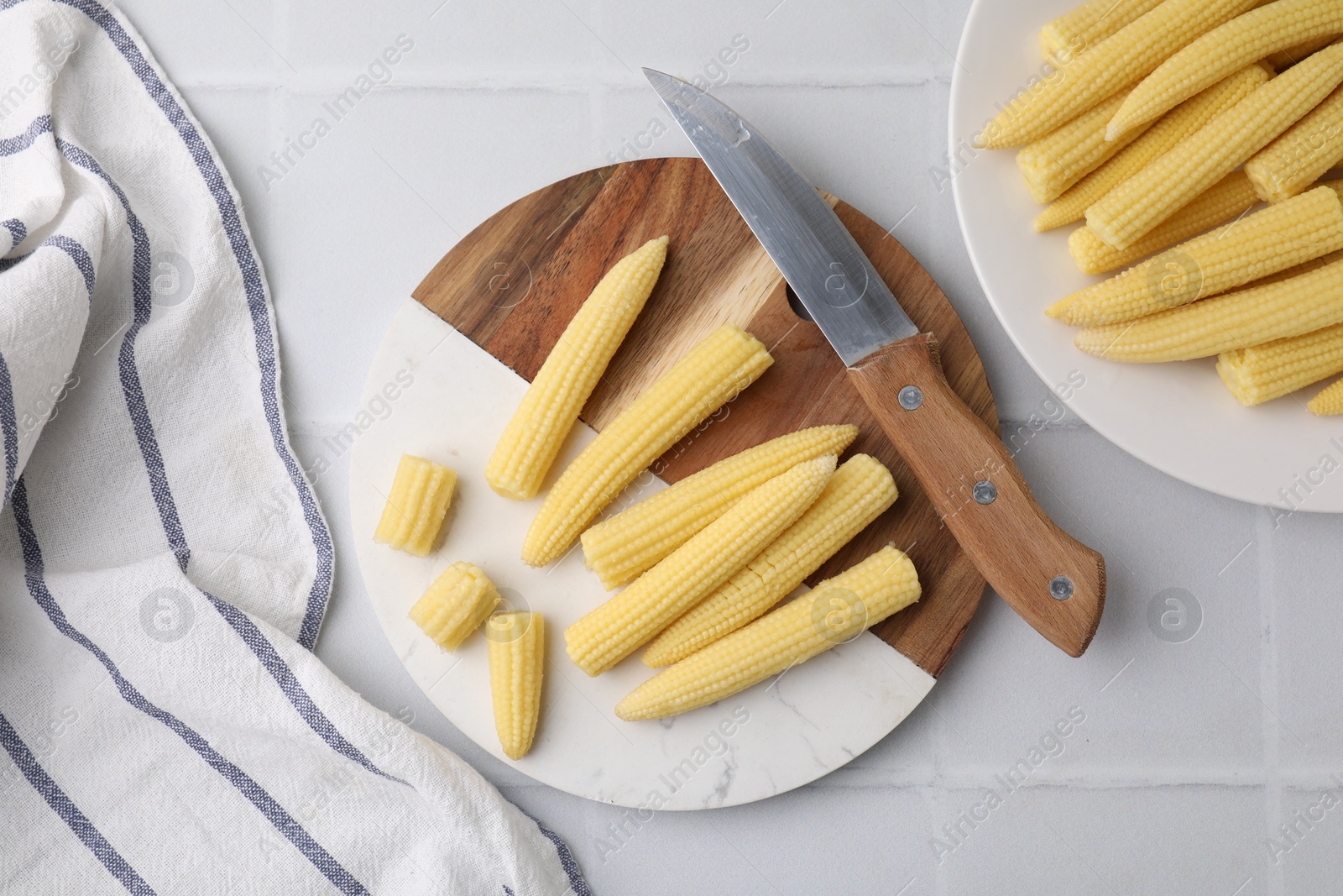 Photo of Tasty fresh yellow baby corns and knife on white tiled table, top view