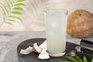 Photo of Glass of coconut water, ice cubes and nuts on grey table
