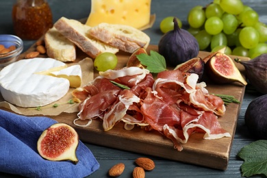 Board with delicious figs, proscuitto, cheese and grapes, closeup