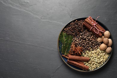 Photo of Different spices, nuts and fir branches on dark gray textured table, top view. Space for text