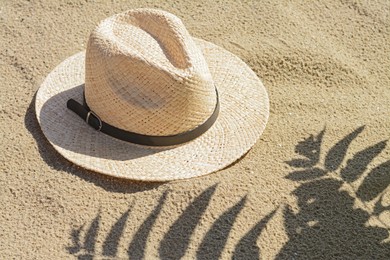 Photo of Stylish straw hat and shadow of beautiful plant on sand outdoors