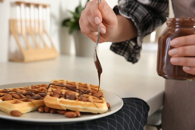 Photo of Woman decorating delicious Belgian waffles with chocolate cream at white countertop in kitchen, closeup