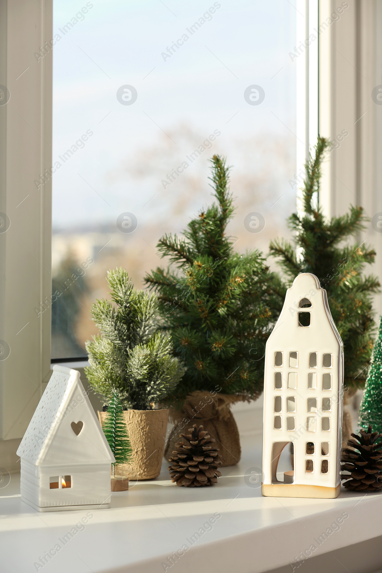 Photo of Beautiful house shaped candle holders and small fir trees on windowsill indoors