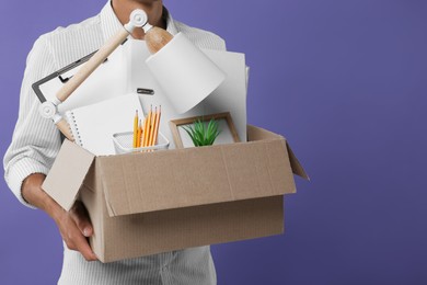 Photo of Unemployed young man with box of personal office belongings on purple background, closeup. Space for text