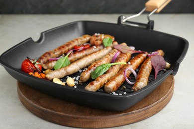 Photo of Grill pan with tasty sausages and vegetables on light table, closeup