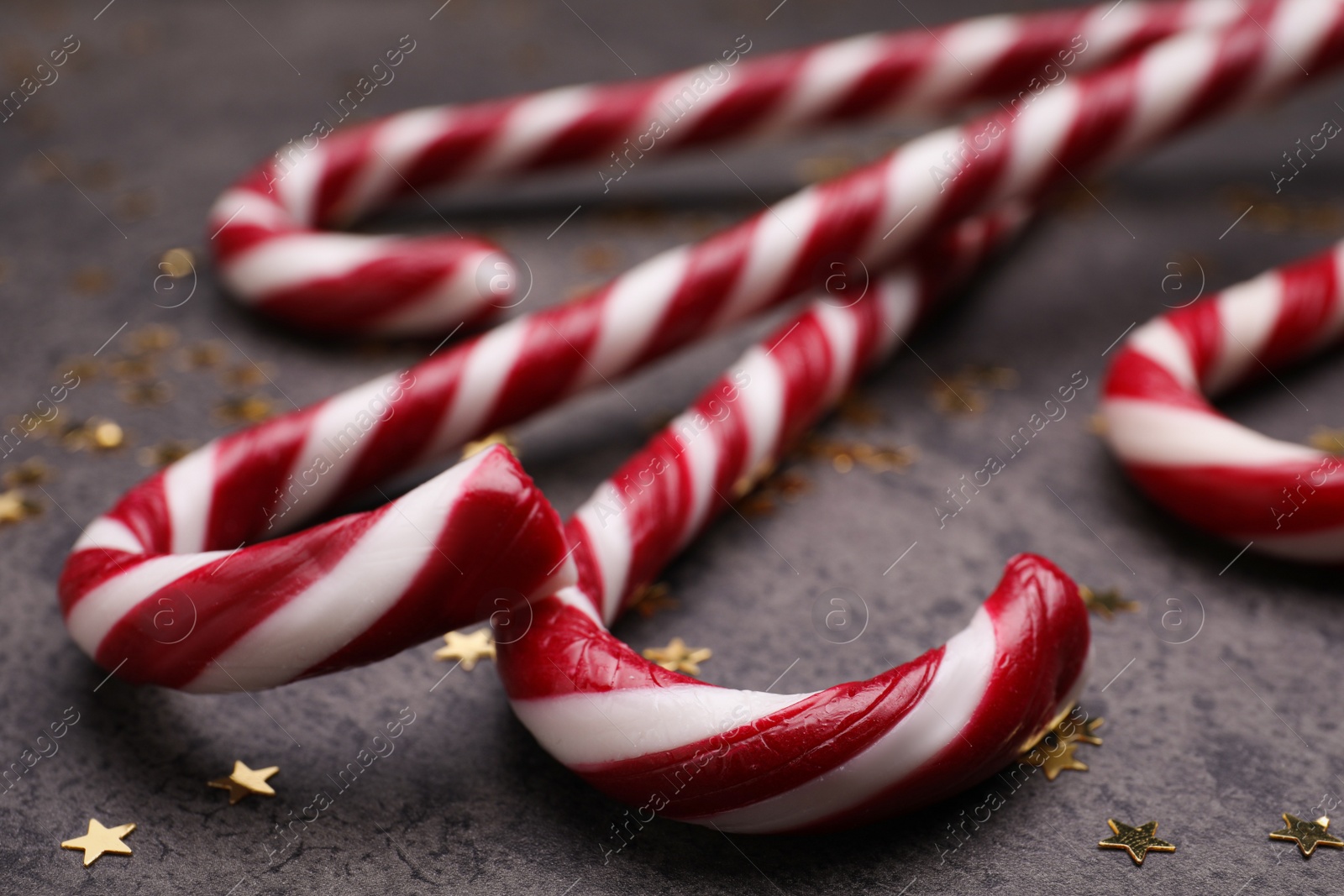 Photo of Many sweet Christmas candy canes and shiny confetti on grey background, closeup