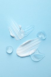Photo of Samples of cosmetic gel and cream on light blue background, top view