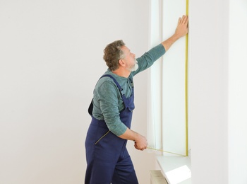 Photo of Service man measuring window for installation indoors. Space for text