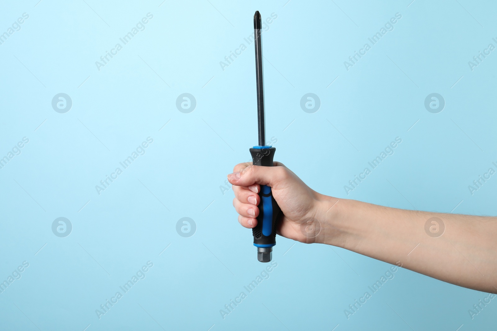 Photo of Woman holding screwdriver on light blue background, closeup