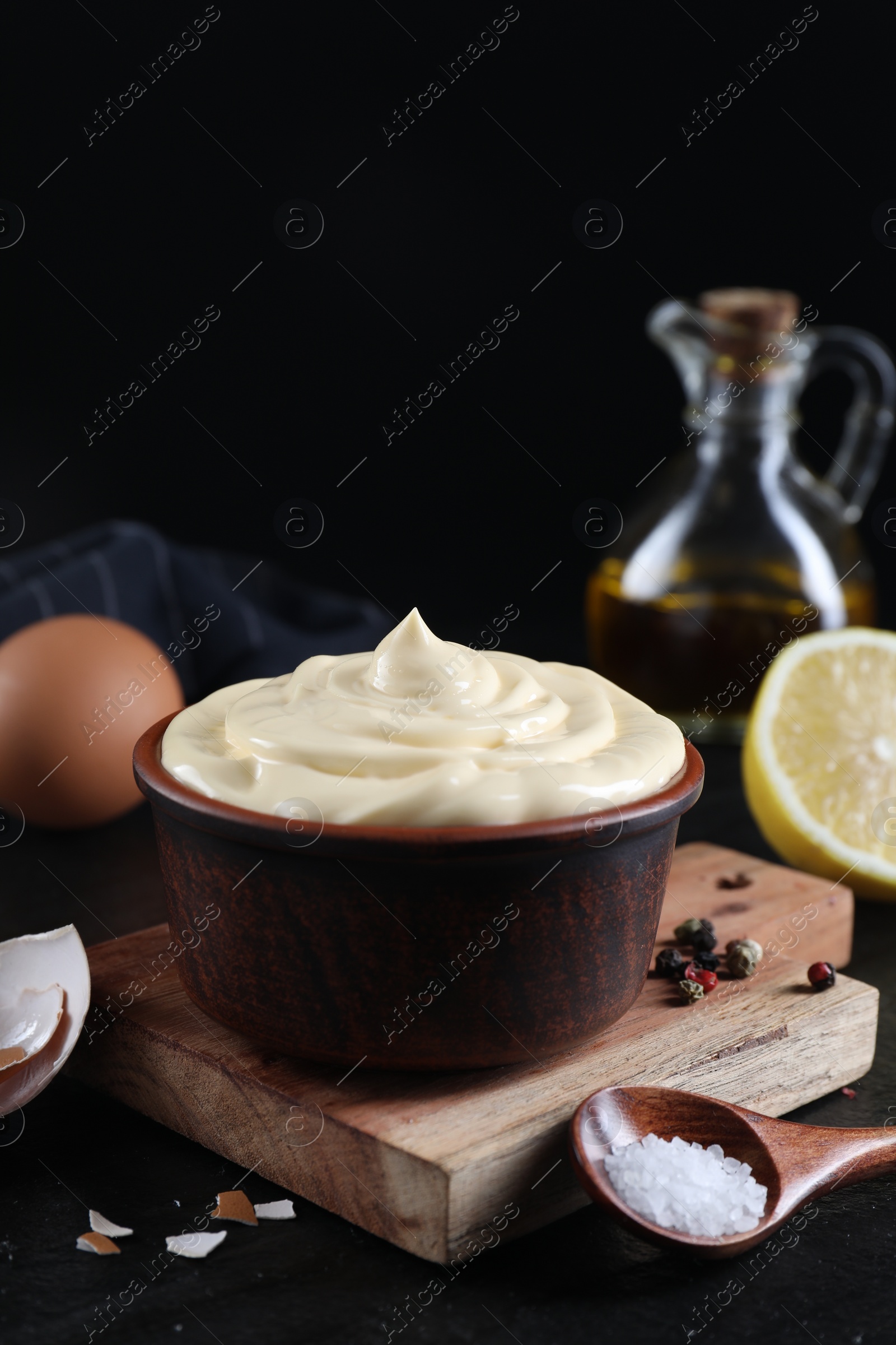 Photo of Fresh mayonnaise sauce in bowl and ingredients on black table, closeup