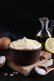 Photo of Fresh mayonnaise sauce in bowl and ingredients on black table, closeup