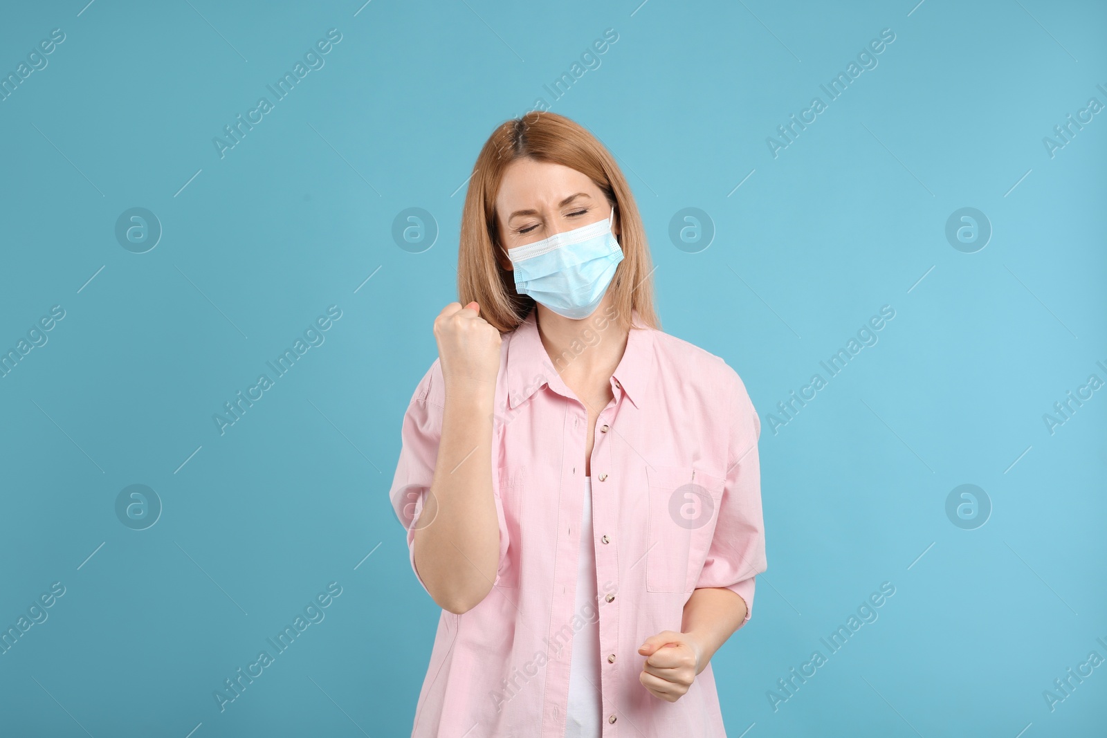 Photo of Emotional woman with protective mask on light blue background. Strong immunity concept