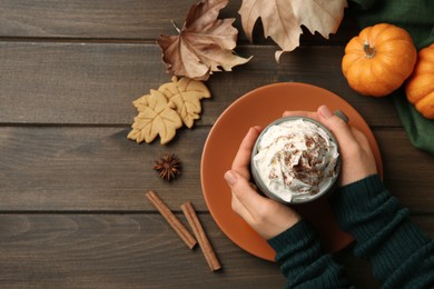 Woman holding cup of tasty pumpkin spice latte with whipped cream at wooden table, top view. Space for text