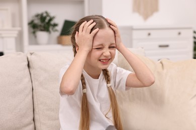 Photo of Little girl suffering from headache on sofa indoors