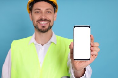 Photo of Male industrial engineer in uniform with phone against light blue background, focus on hand