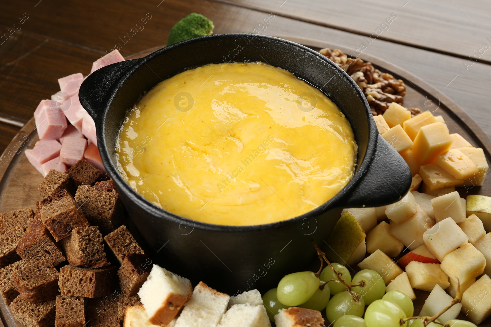 Photo of Fondue pot with melted cheese and different products on wooden table, closeup