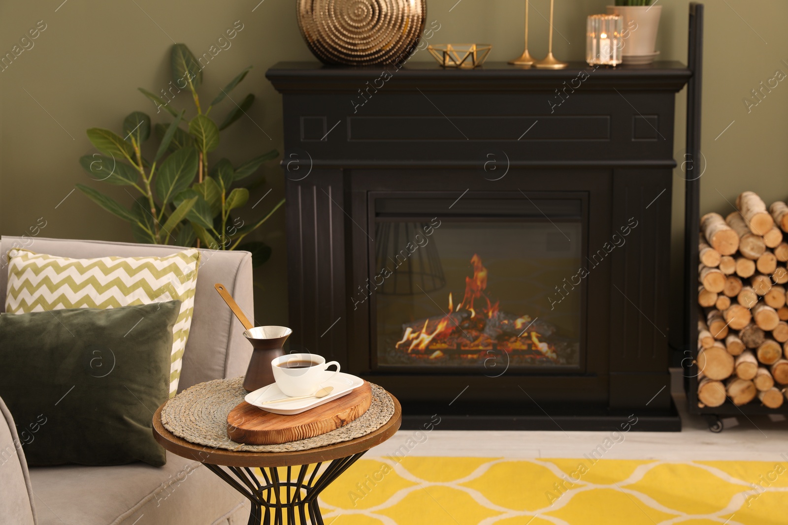 Photo of Cup of coffee and cezve on table near fireplace in living room