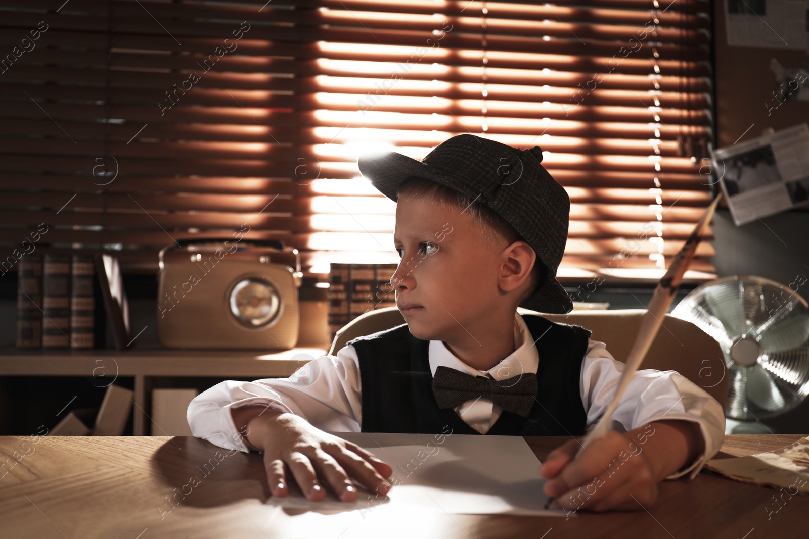 Photo of Cute little detective writing with feather at table in office