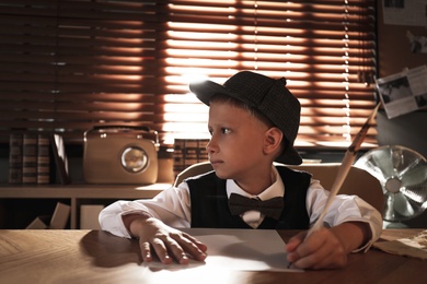 Photo of Cute little detective writing with feather at table in office