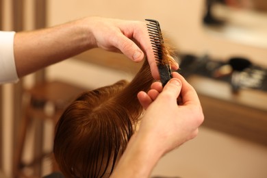Photo of Professional hairdresser combing boy's hair in beauty salon, closeup