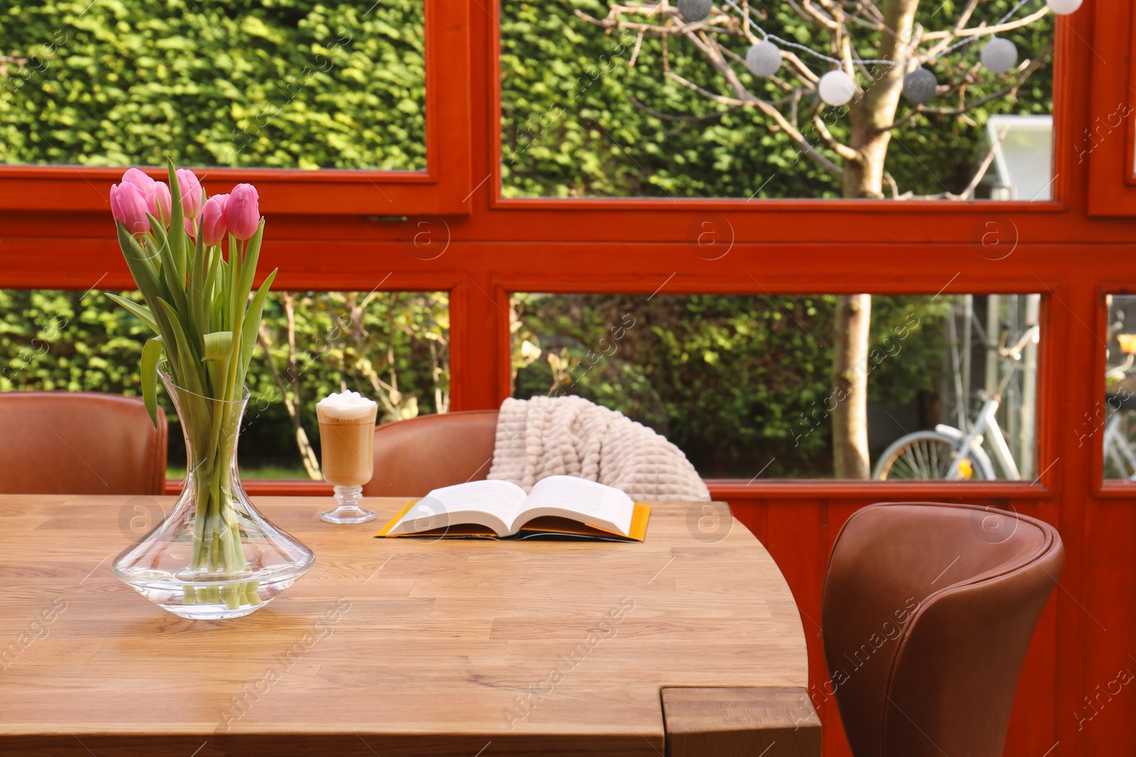 Photo of Glass of delicious cocoa, pink tulips and book on wooden table at terrace