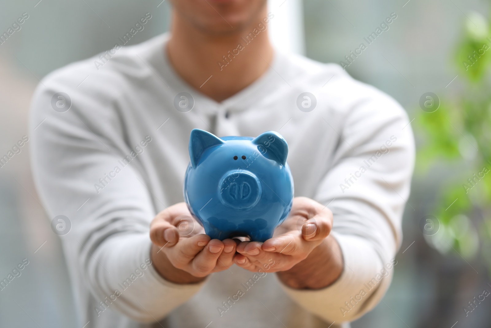 Photo of Man holding piggy bank against blurred background, closeup