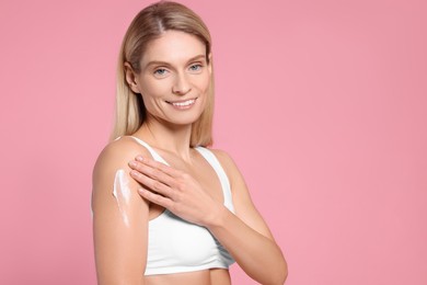 Photo of Woman applying body cream onto her arm against pink background, space for text