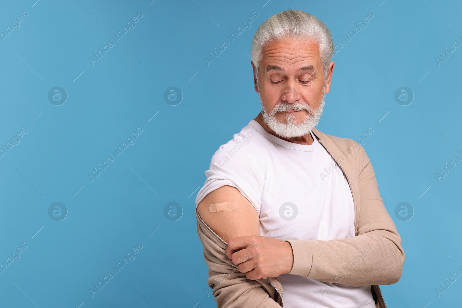 Photo of Senior man with adhesive bandage on his arm after vaccination against light blue background, space for text