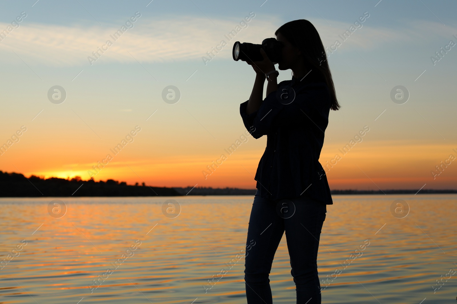 Photo of Young female photographer taking photo of riverside sunset with professional camera outdoors