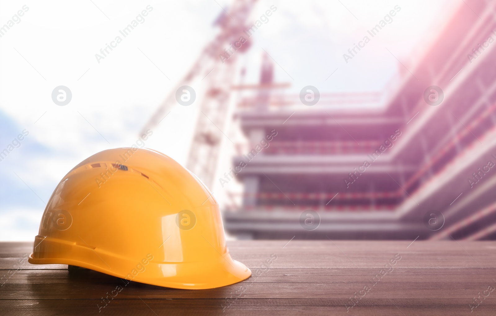 Image of Hard hat on wooden surface at construction site with unfinished building. Space for text 