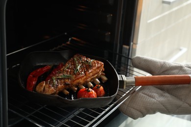 Photo of Chef taking pan with delicious roasted ribs out of oven, closeup