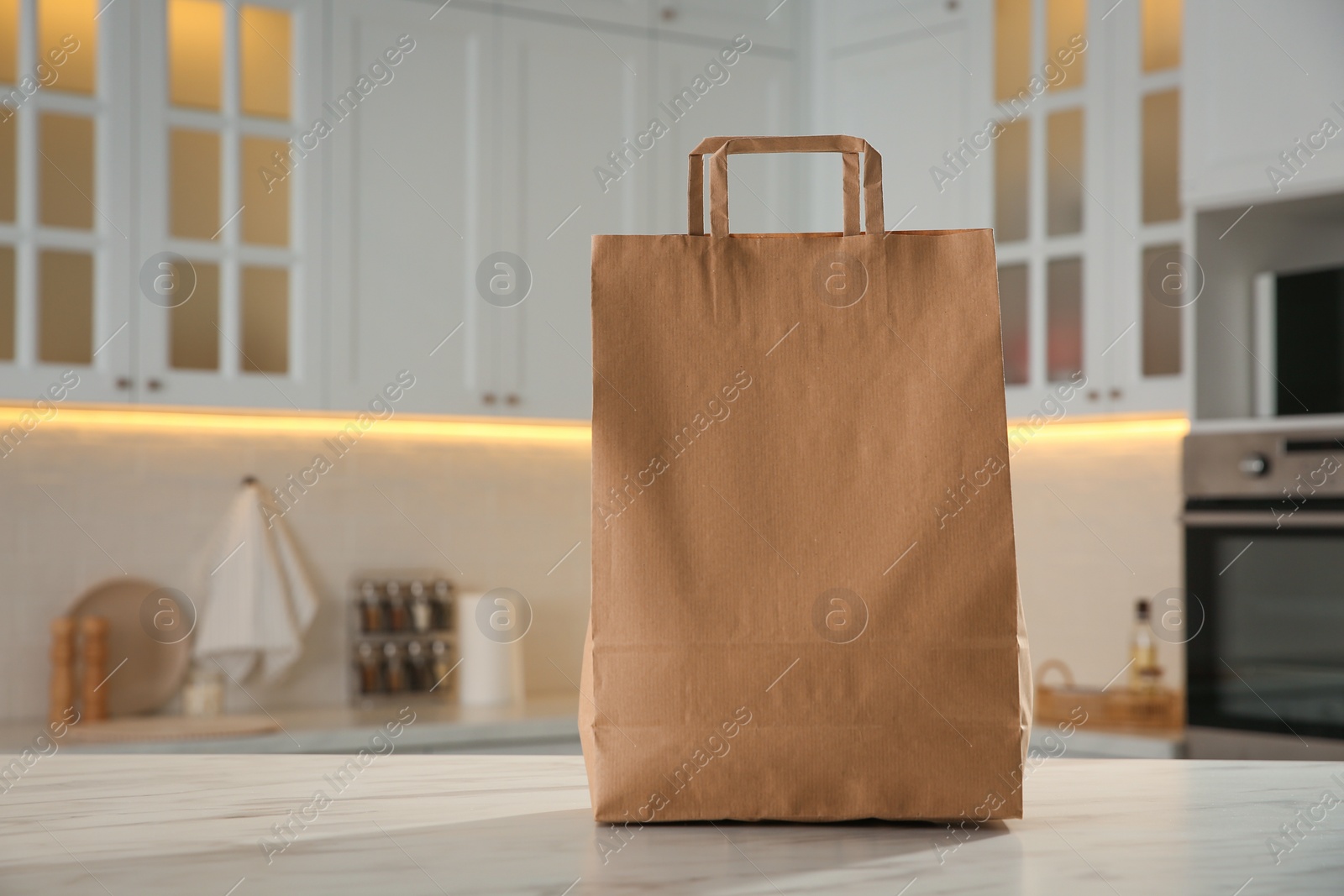 Photo of Paper shopping bag on white marble table in kitchen. Space for text