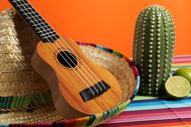 Composition with Mexican sombrero hat and ukulele on color table, closeup