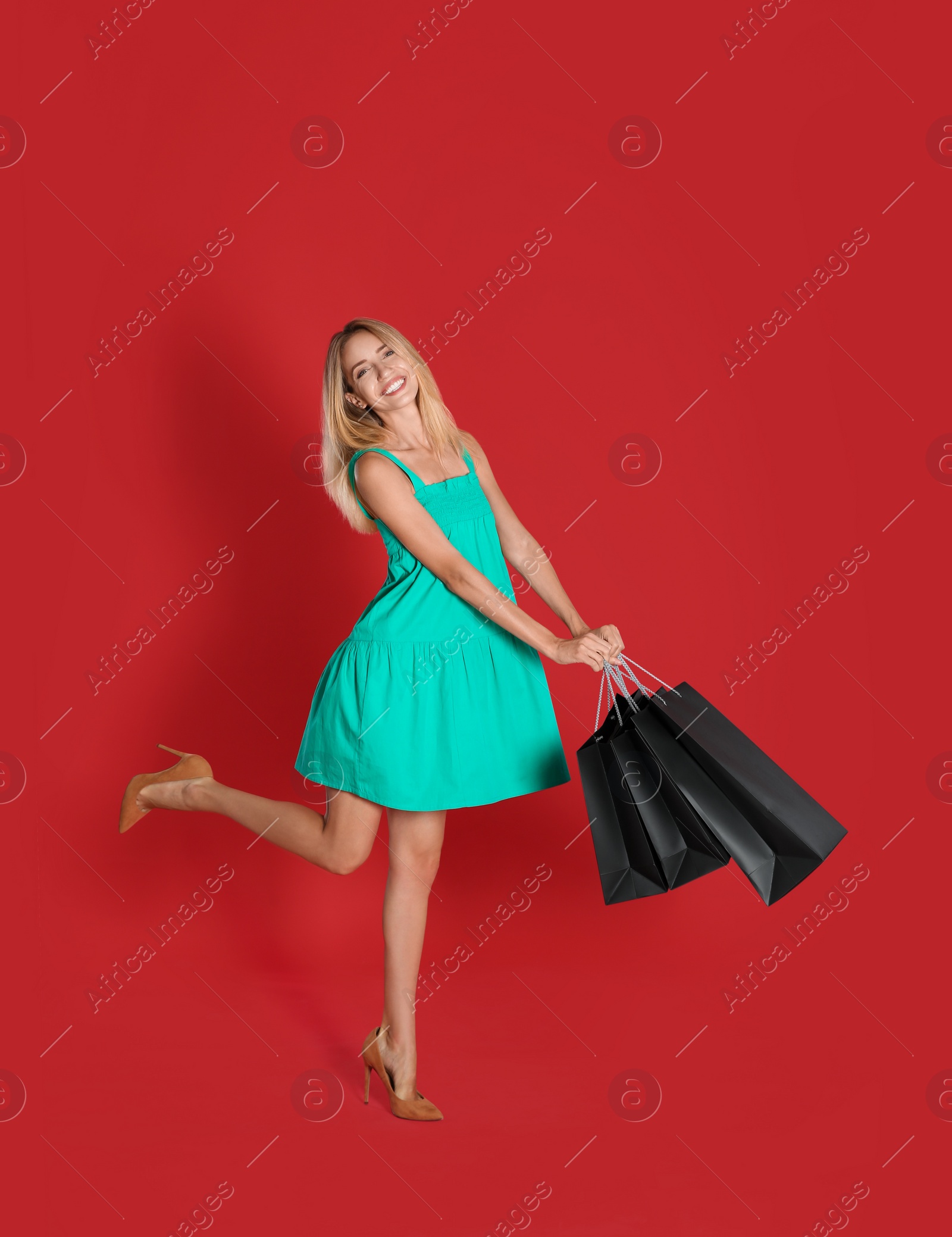 Photo of Happy young woman with shopping bags on red background. Black Friday Sale