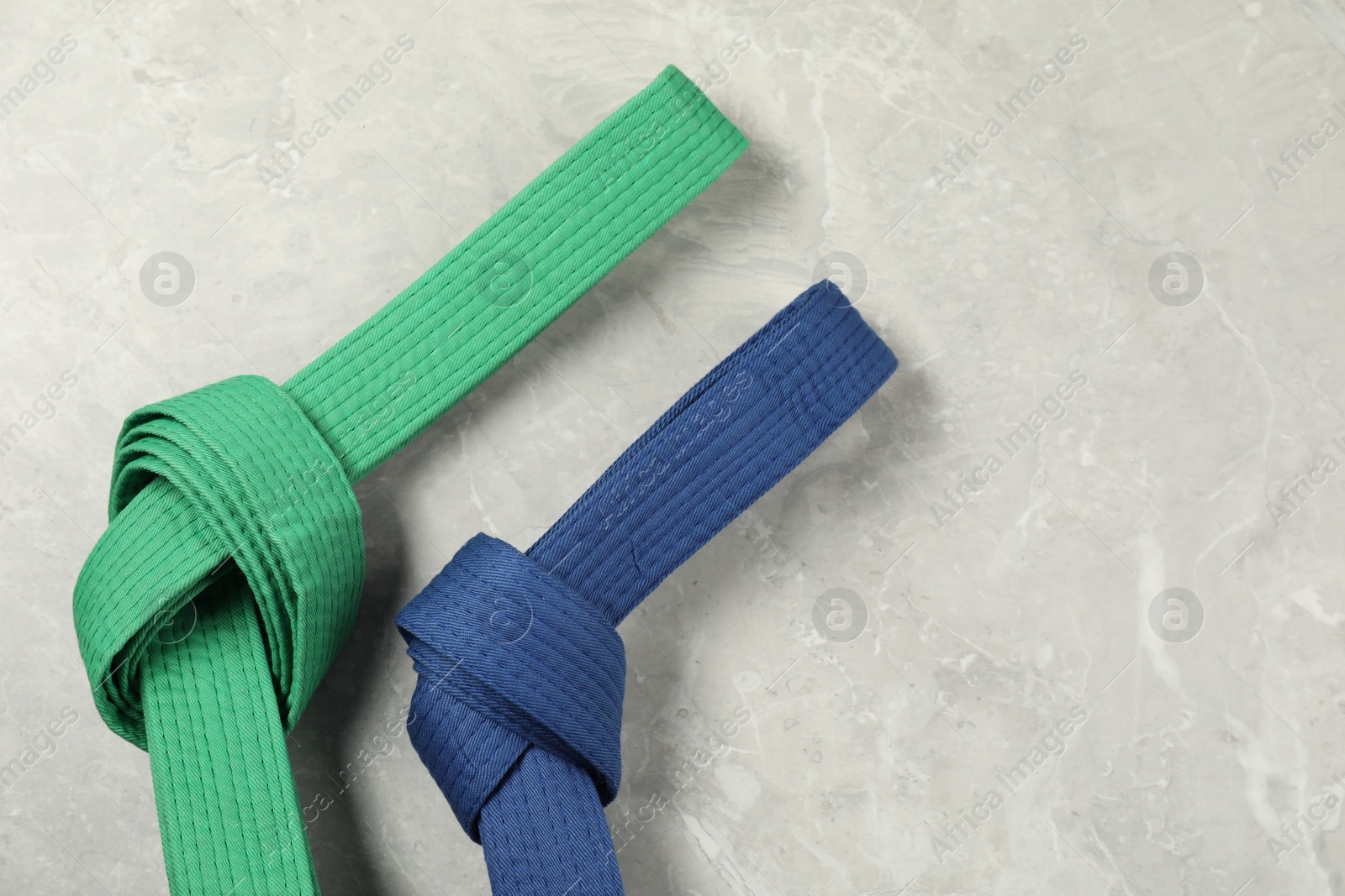 Photo of Green and blue karate belts on gray marble background, flat lay. Space for text