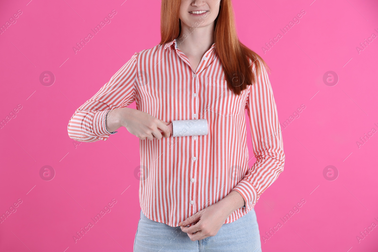 Photo of Young woman cleaning clothes with lint roller on pink background, closeup