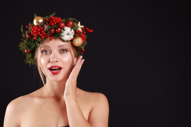 Photo of Beautiful young woman wearing Christmas wreath on black background. Space for text