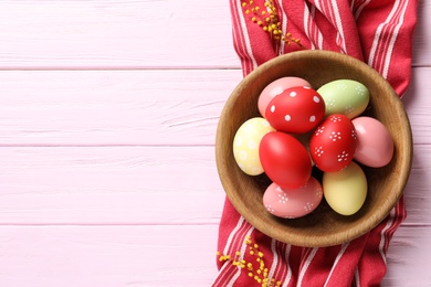 Photo of Bowl with painted Easter eggs and napkin on wooden table, flat lay. Space for text