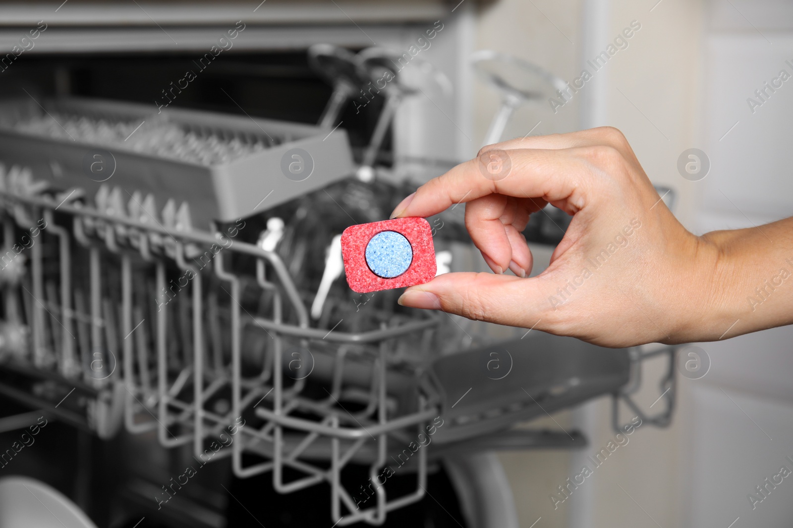 Photo of Woman putting detergent tablet into open dishwasher in kitchen, closeup