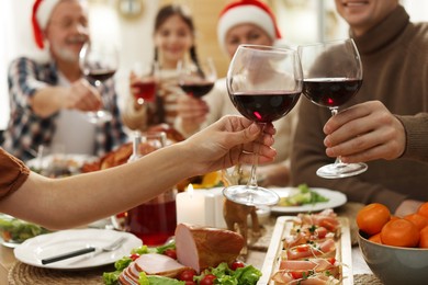 Photo of Family clinking glasses of wine at festive dinner, focus on hands. Christmas celebration