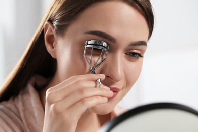 Young woman using eyelash curler near mirror, closeup