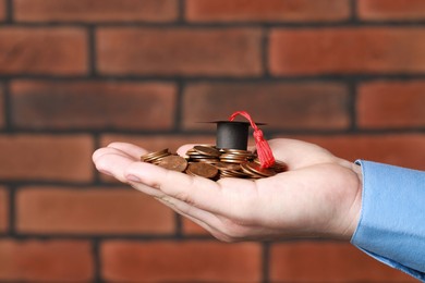 Photo of Man holding coins and graduation cap against brick background, closeup. Scholarship concept